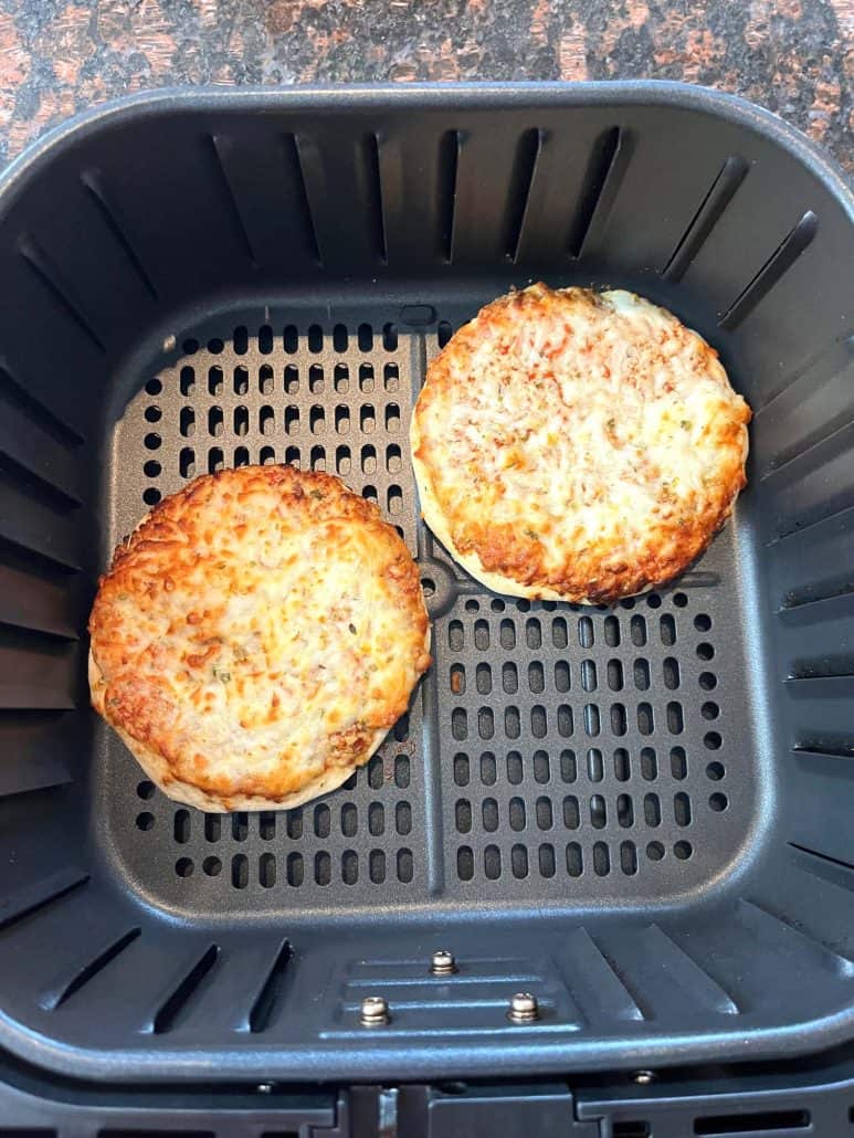 Two golden brown Trader Joe’s Bambino Pizzas inside an air fryer basket, showing how perfectly they cook.