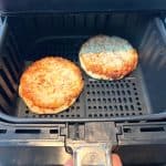 Two golden brown frozen breakfast sandwiches cooking in an air fryer basket, showing how perfectly they crisp up using this easy air fryer method.
