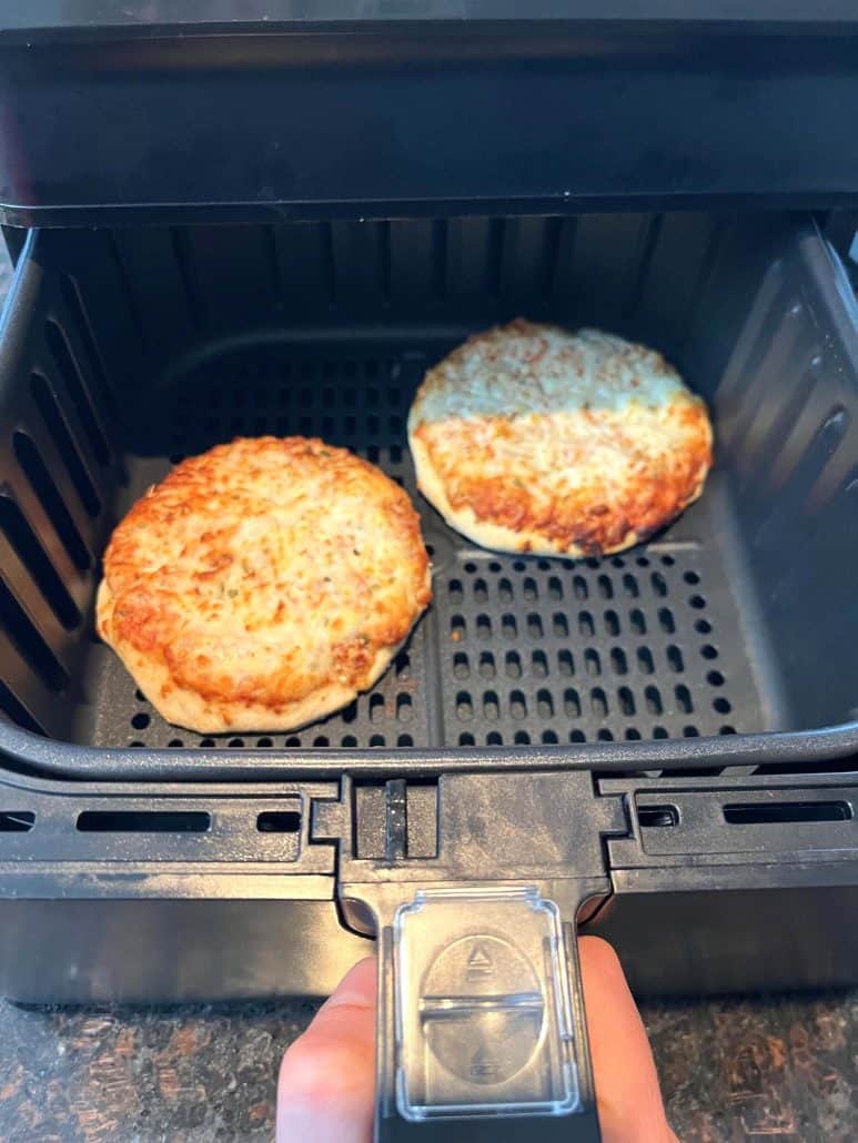 Two golden brown frozen breakfast sandwiches cooking in an air fryer basket, showing how perfectly they crisp up using this easy air fryer method.