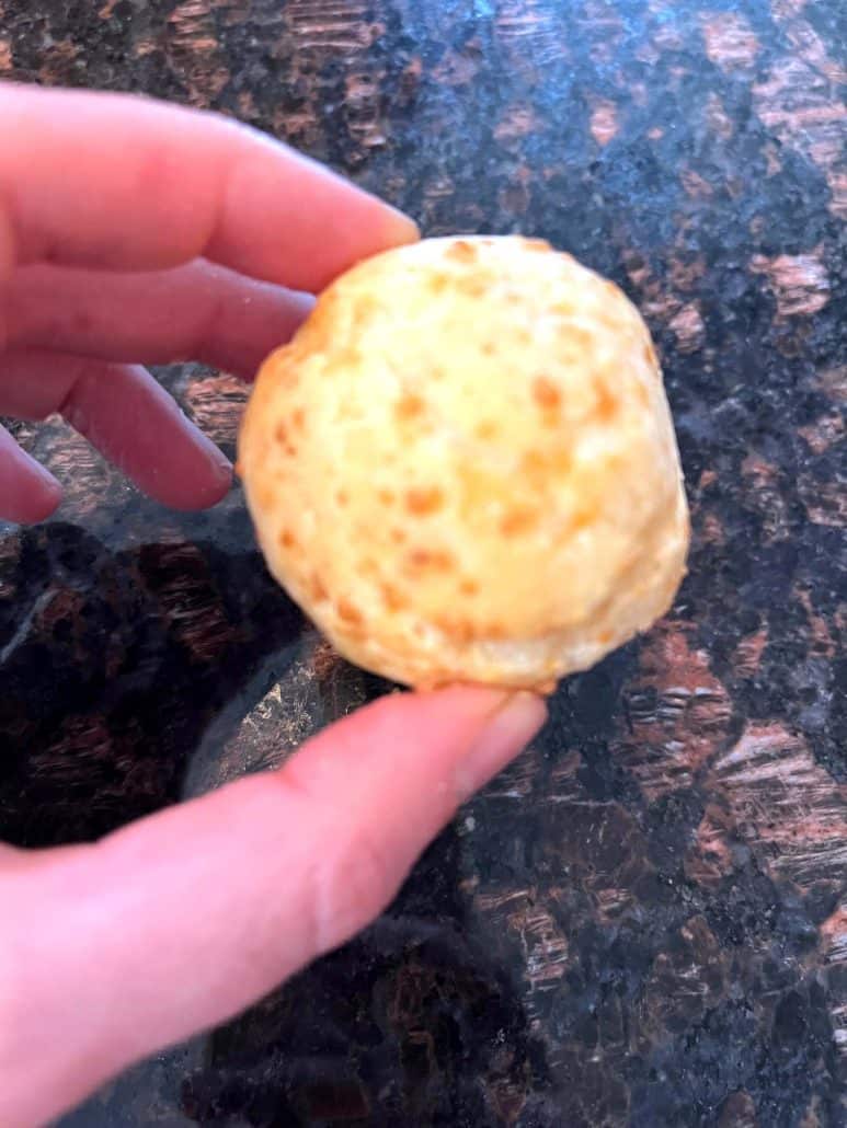 Melanie Mendelson from melaniecooks.com is holding a perfectly cooked Brazilian cheese bread, showing its golden and airy texture. Ideal for a quick air fryer snack or appetizer.
