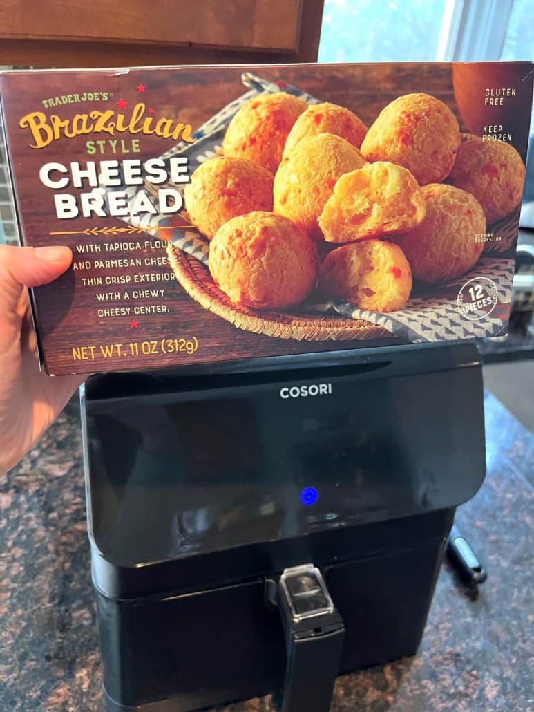 Melanie Mendelson from melaniecooks.com is holding a box of Trader Joe’s Brazilian Cheese Bread in front of an air fryer, getting ready to cook the cheese bread for a quick and easy snack.