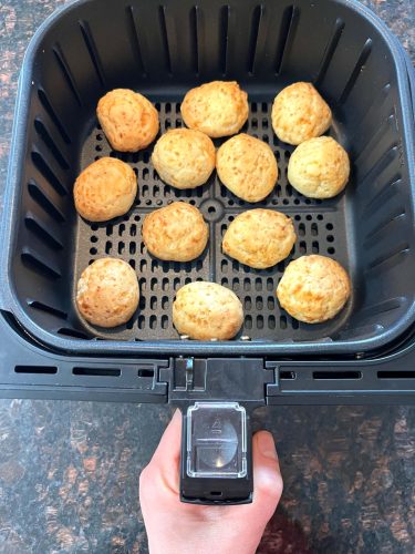 Air fryer basket filled with golden brown Brazilian cheese bread, cooked perfectly crispy on the outside.