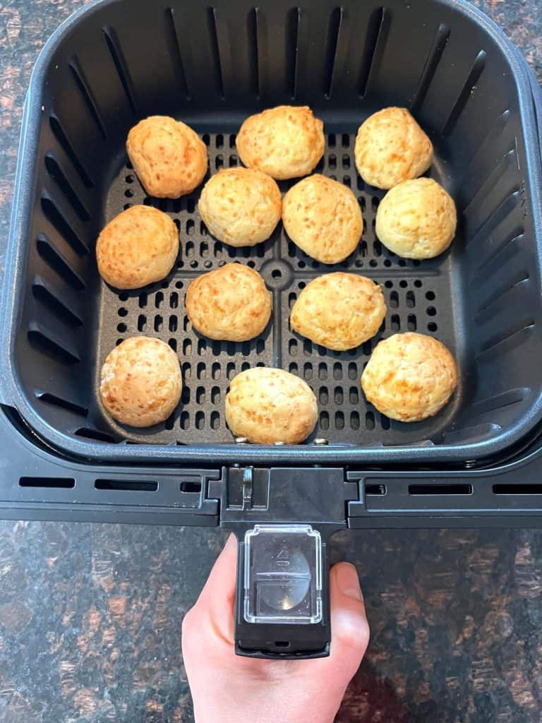 Air fryer basket filled with golden brown Brazilian cheese bread, cooked perfectly crispy on the outside.