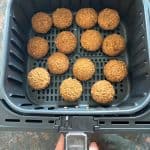 Falafel cooking in an air fryer basket, perfectly crisp and golden brown. Just like in the easy Trader Joe’s Frozen Falafel Air Fryer recipe.