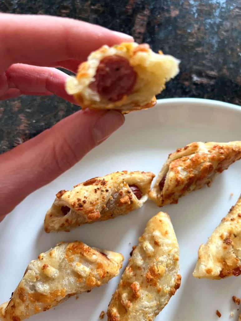 Hand of Melanie Mendelson from melaniecooks.com, holding a bitten Trader Joe's Pastry Pup, showing the juicy hot dog inside flaky pastry.