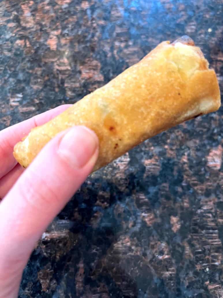 Melanie Mendelson from melaniecooks.com holding a crispy Trader Joe’s Chicken Spring Roll, showing the golden brown texture after air frying.