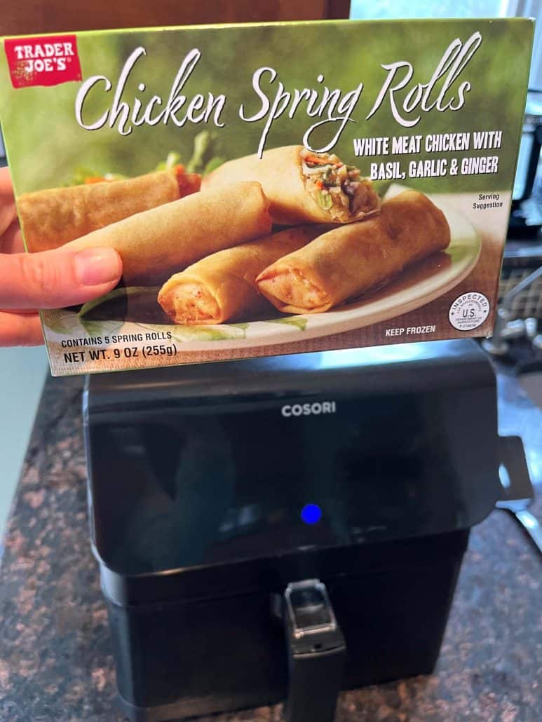 Trader Joe’s Chicken Spring Rolls held above an air fryer—showing the easy way to cook these frozen spring rolls to crispy perfection.