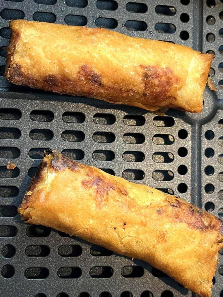 Close-up of golden brown Trader Joe’s Chicken Spring Rolls in the air fryer basket—showing their crispy texture.