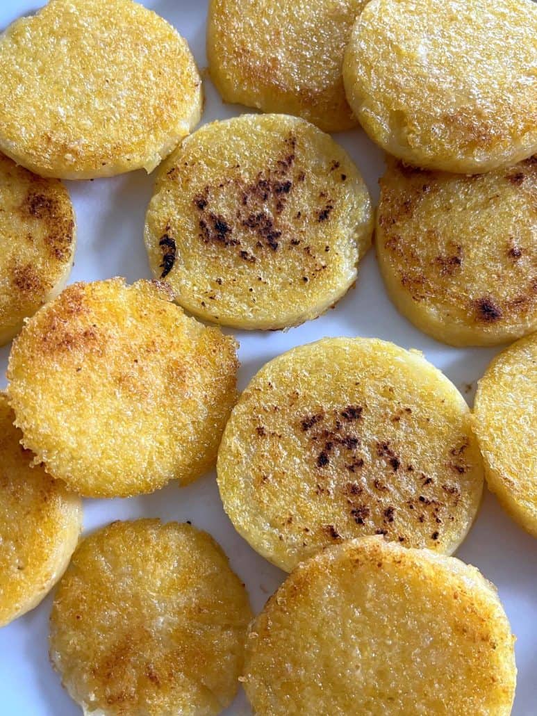 Close-up of crispy fried polenta slices on a plate, showing their golden texture with a slight caramelization on the edges.