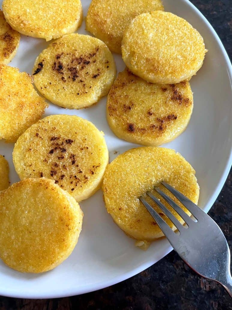 A fork placed next to a plate of crispy fried polenta slices, ready to be enjoyed, showing the golden-brown texture and soft interior.
