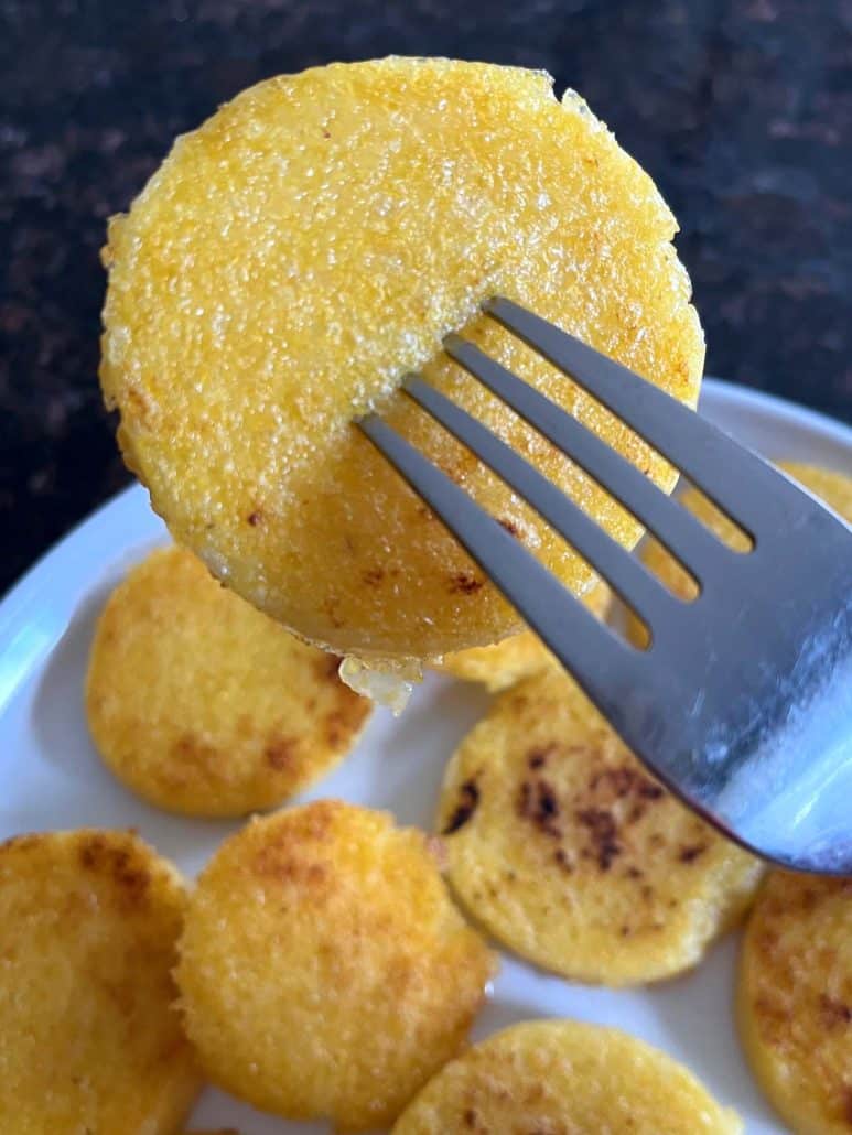 A fork lifting a crispy fried polenta slice from a plate, showcasing its golden brown texture, ready to be enjoy.