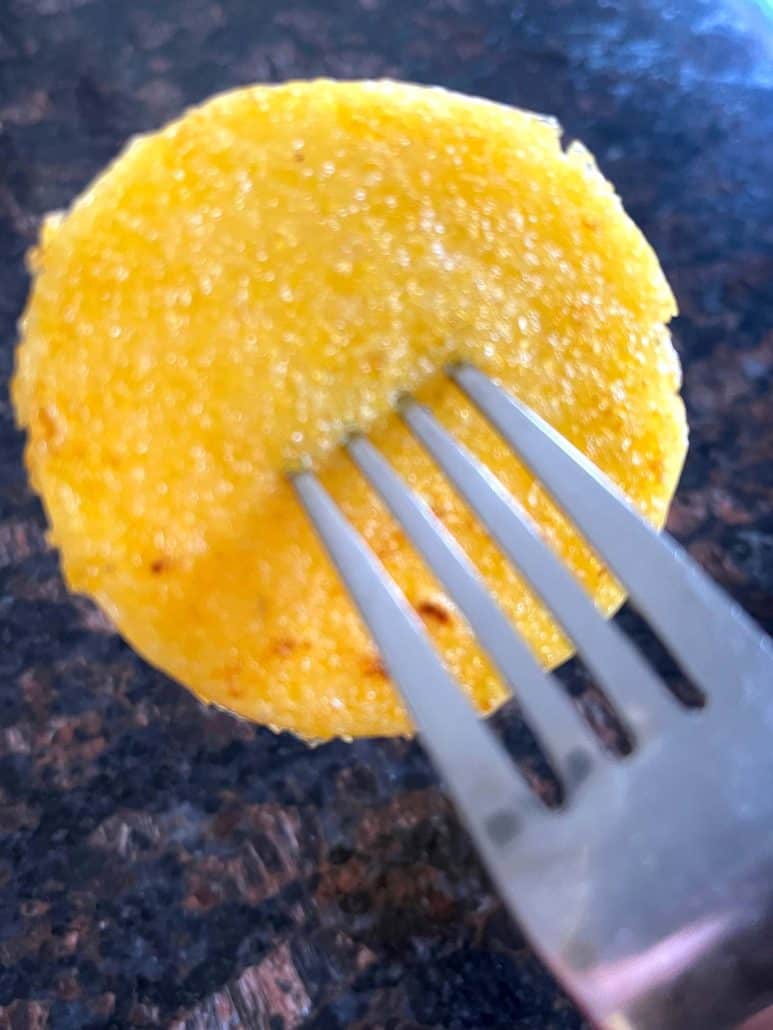 Close-up of a fork piercing a crispy fried polenta slice, highlighting its golden texture and slightly crunchy edges.