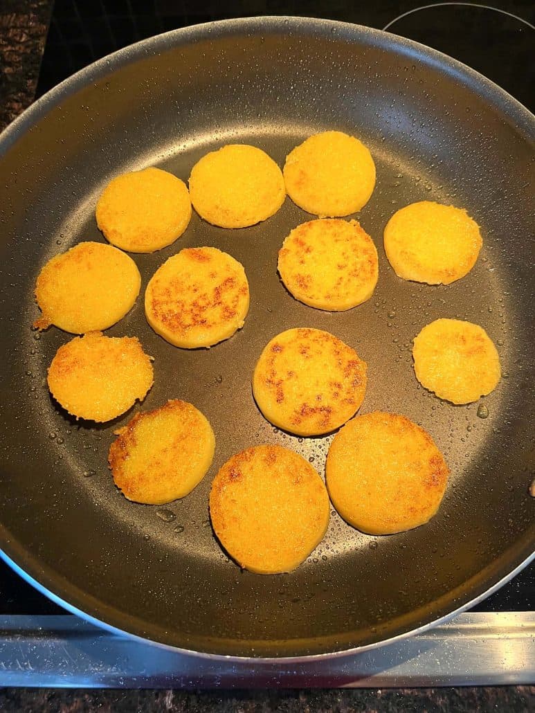 Golden brown crispy polenta slices frying in a pan, with a perfectly crispy texture forming on both sides.