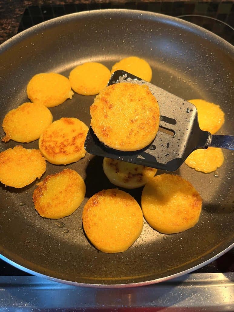 Lifting a crispy fried polenta slice with a spatula from the pan, showing its golden brown crust.