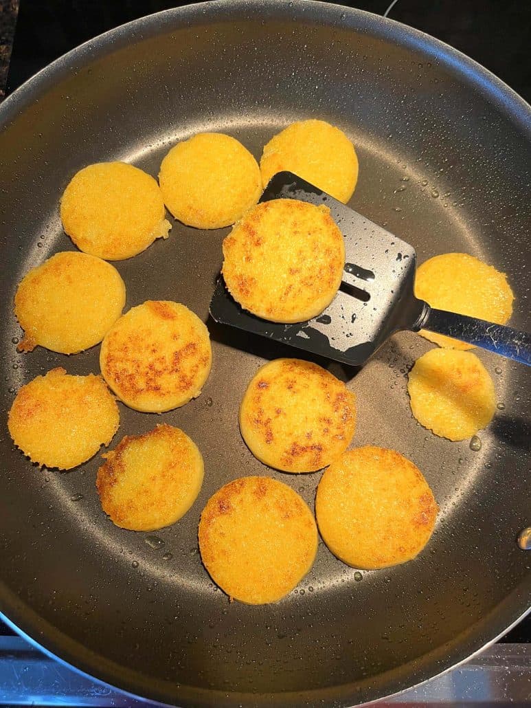 Flipping crispy polenta slices in a frying pan with a spatula, showing the golden brown color on one side, as part of the Crispy Fried Polenta Slices recipe.