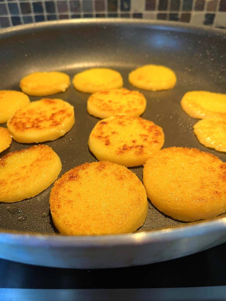 Pre-cooked polenta slices frying in a pan, turning golden brown and crispy on one side.