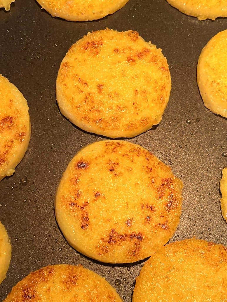 Close-up of perfectly golden brown and crispy fried polenta slices in a pan, showcasing their delicious texture.