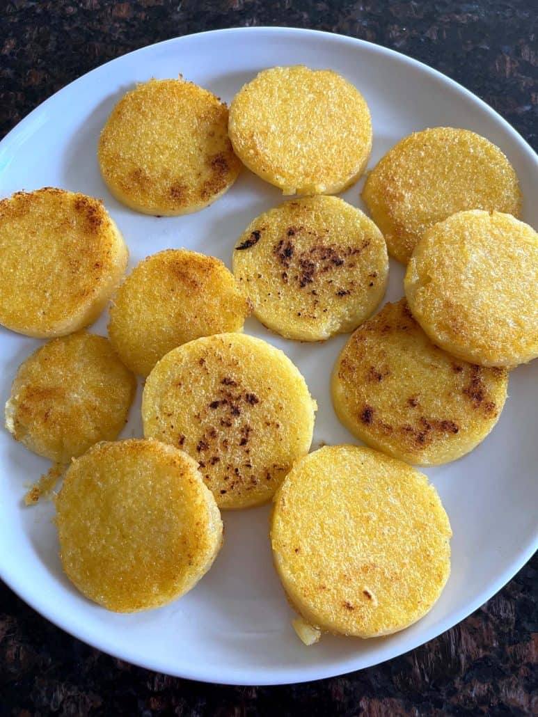 Golden, crispy fried polenta slices arranged on a white plate, showcasing the perfect texture of the crispy edges and soft interior.