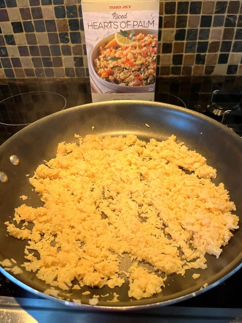 Hearts of palm rice cooking in a non-stick skillet with the Trader Joe’s box in the background – a simple stovetop method for a quick low-carb side dish.