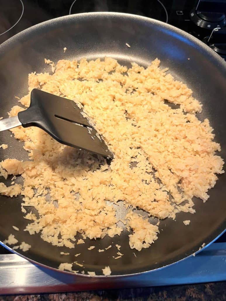 Cooking hearts of palm rice in a skillet while breaking it up with a spatula – quick and healthy stovetop rice alternative.