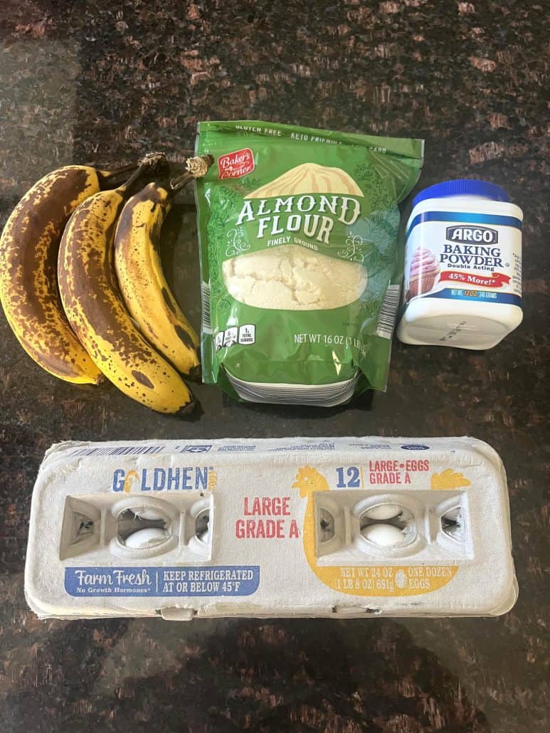 Ingredients for almond flour banana bread recipe including ripe bananas, almond flour, baking powder, and eggs on a kitchen counter.