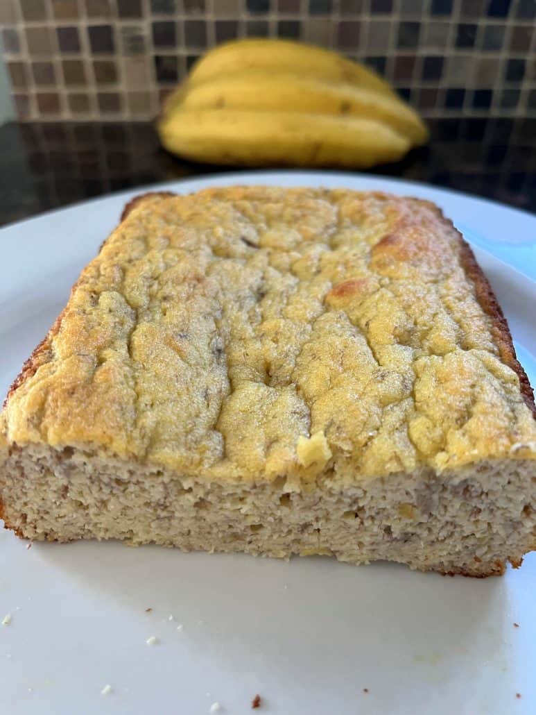 Close-up of gluten-free almond flour banana bread on a plate with ripe bananas in the background.