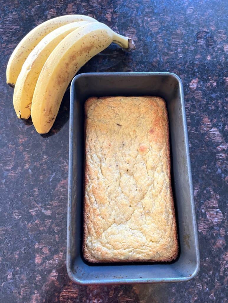 Freshly baked almond flour banana bread in a loaf pan next to ripe bananas.