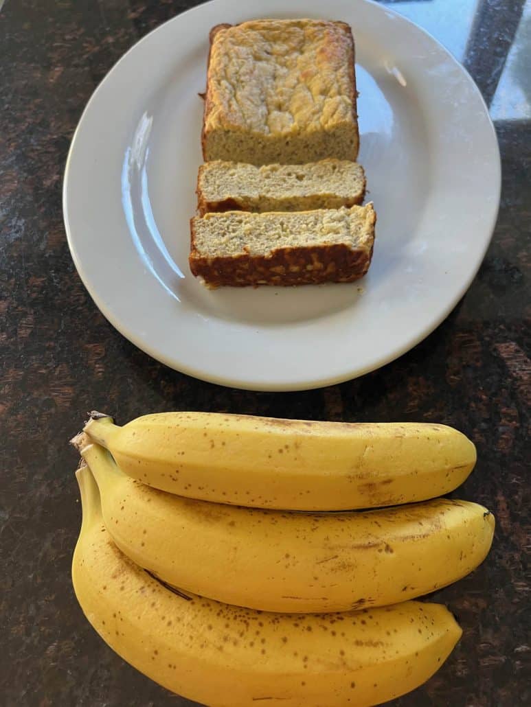 Sliced almond flour banana bread on a white plate with ripe bananas displayed underneath, showcasing ingredients and finished recipe.
