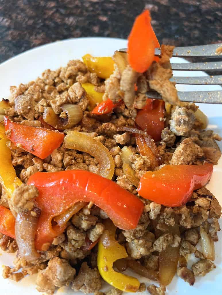 Fork picking up a bite of ground turkey fajitas with sautéed bell peppers and onions, served on a white plate.