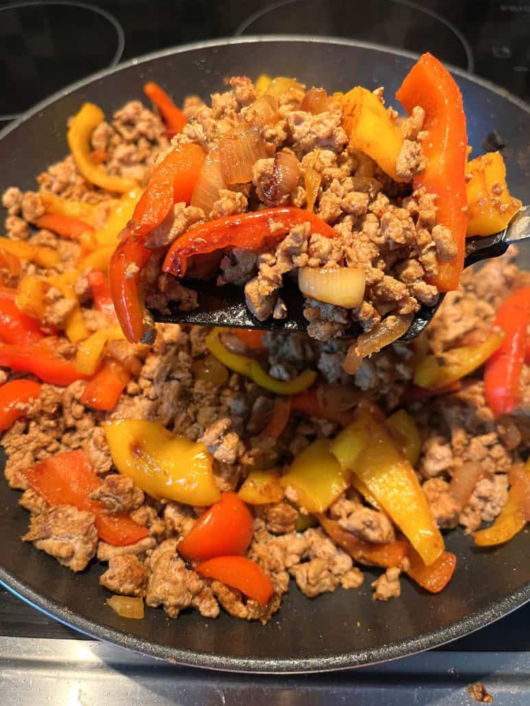 Scooping a serving of cooked ground turkey fajitas from the skillet, with colorful bell peppers and onions mixed in.