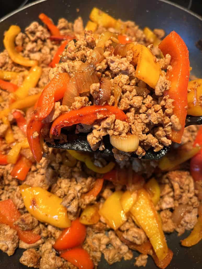 Close-up of ground turkey fajitas being lifted from the skillet, highlighting the seasoned meat and sautéed peppers.