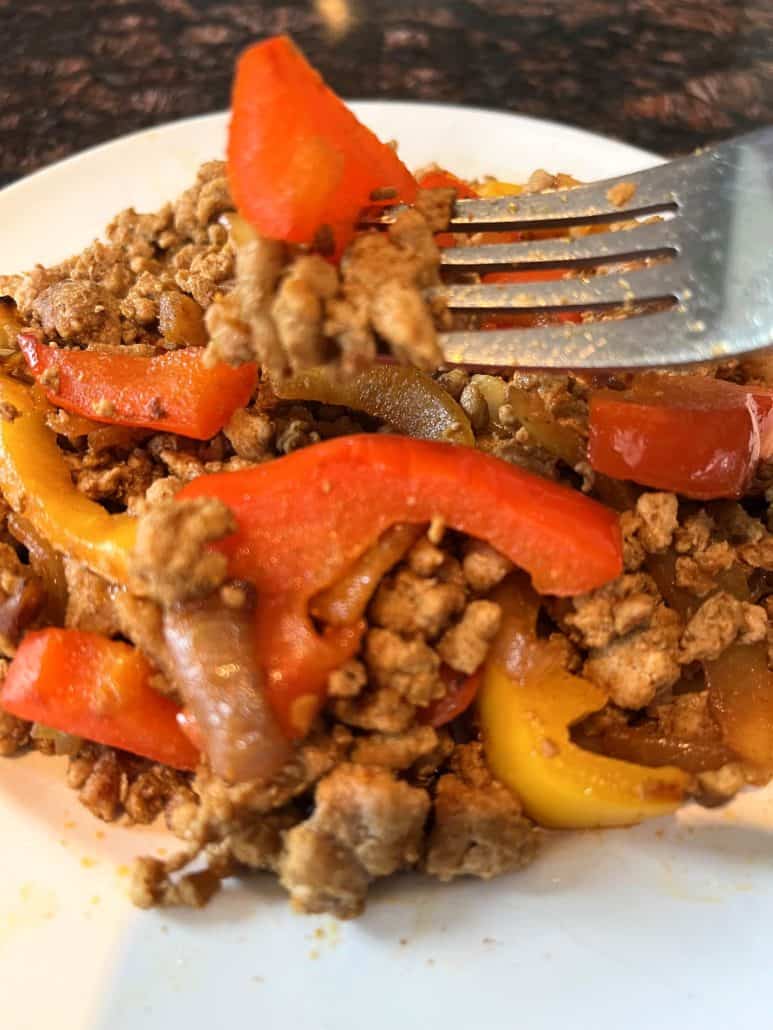 Forkful of ground turkey fajitas with red and yellow bell peppers on a plate, showing the final served dish from the recipe.
