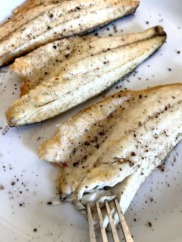 Fork flaking into seasoned branzino fillets on a plate, showing the tender texture from the Air Fryer Branzino Fillets recipe.