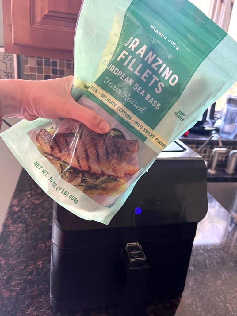 Holding a package of frozen Trader Joe’s branzino fillets in front of an air fryer, ready to make the Air Fryer Branzino Fillets recipe.