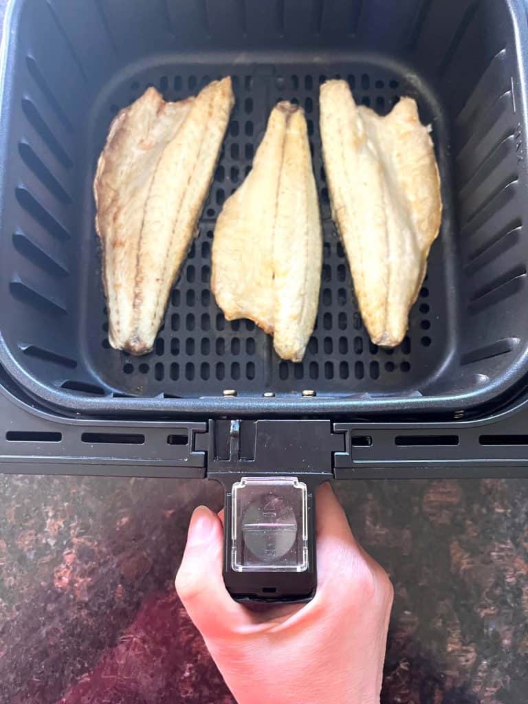 Three frozen branzino fillets cooking in an air fryer basket as shown in the Air Fryer Branzino Fillets recipe.