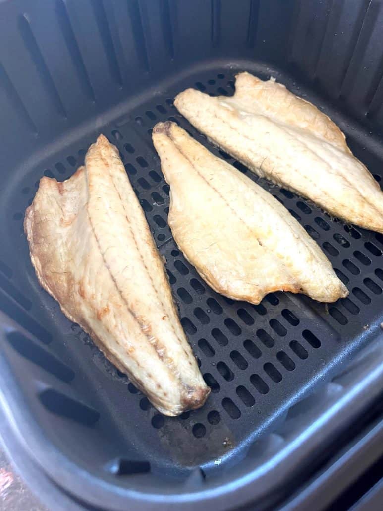 Side view of three branzino fillets cooked in an air fryer basket, part of the Air Fryer Branzino Fillets step-by-step recipe.
