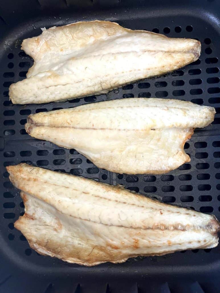 Close-up of three golden brown branzino fillets cooked in the air fryer basket, featured in the Air Fryer Branzino Fillets recipe.