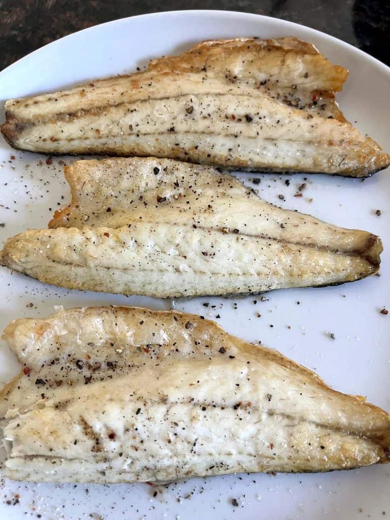 Four cooked and seasoned branzino fillets on a white plate, ready to serve from the Air Fryer Branzino Fillets recipe.