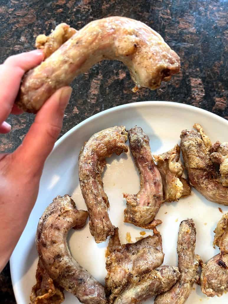 Hand holding a crispy air-fried chicken neck above a plate of cooked necks, showcasing the final result of the Air Fryer Chicken Necks recipe.