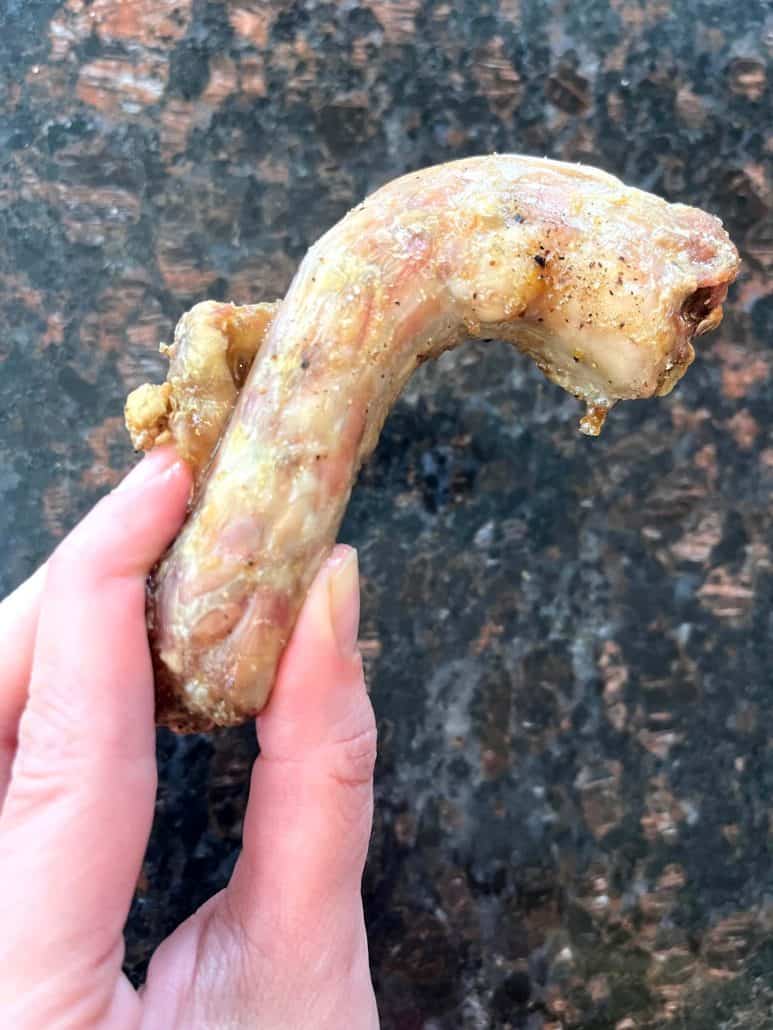 Close-up of a hand holding a crispy cooked chicken neck, showing the golden texture from the Air Fryer Chicken Necks recipe.