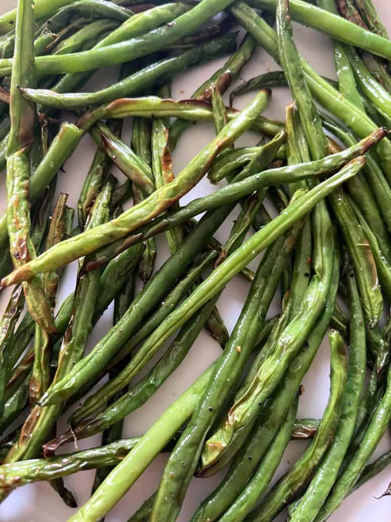 Close-up view of crispy roasted French green beans (Haricot Verts) on a white plate, showcasing their golden edges and perfect texture from the air fryer.