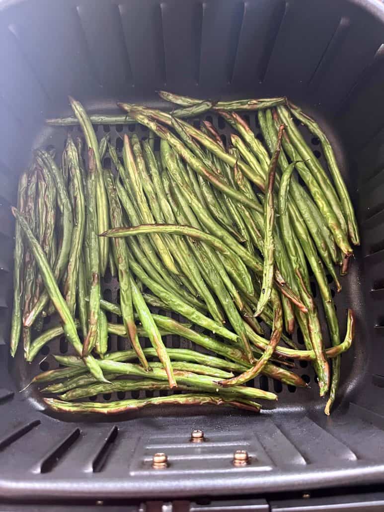Air fryer basket filled with evenly roasted French green beans (Haricot Verts), showing the finished result.