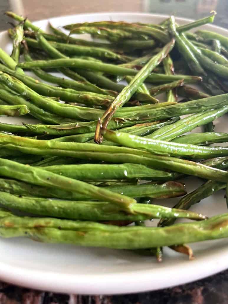 Crispy air-fried French green beans (Haricot Verts) served on a white plate, highlighting their roasted texture and golden edges.