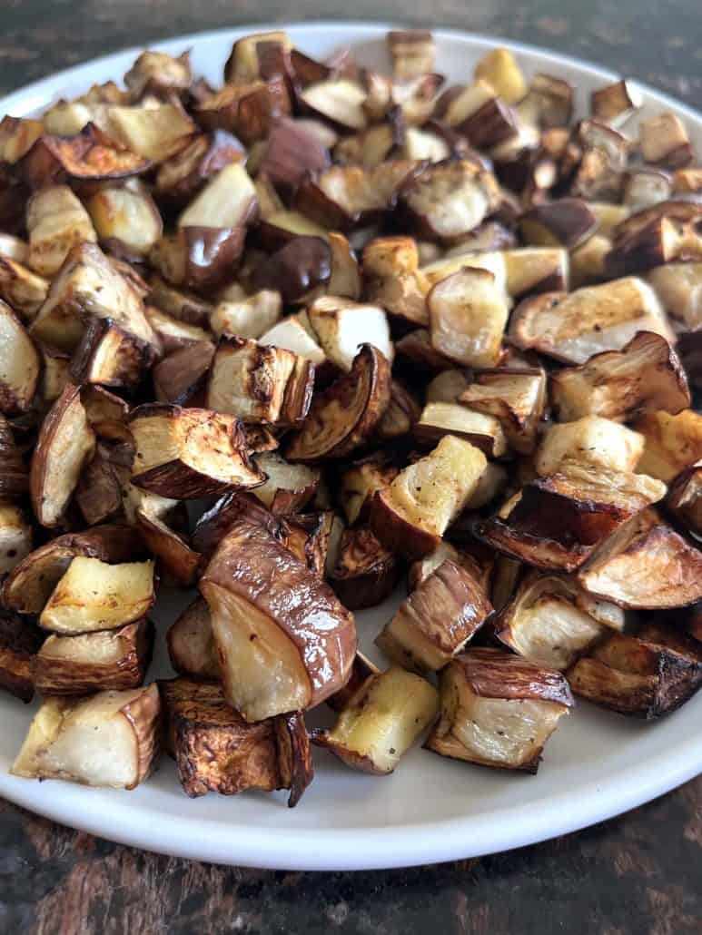 Side view of golden-brown air-fried graffiti eggplant cubes served on a white plate, showing the crispy texture.