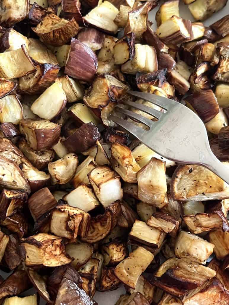 Fork nestled into a plate of golden air-fried graffiti eggplant cubes, capturing the crispy texture.