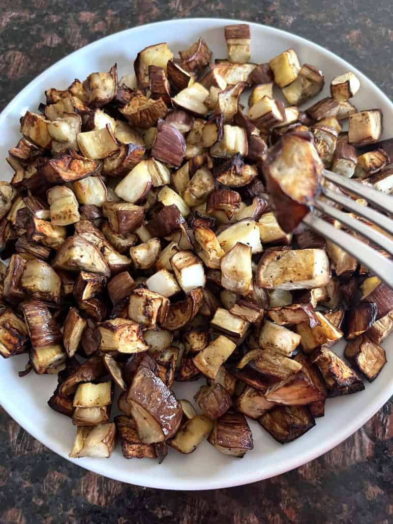Fork picking up a bite of crispy air-fried graffiti eggplant from a white plate, showcasing the tender texture.