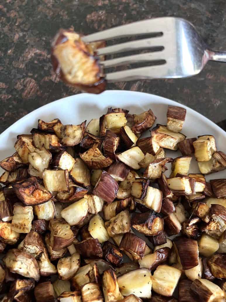 Fork holding a bite-sized piece of crispy graffiti eggplant above a plateful, showing off the perfect texture.