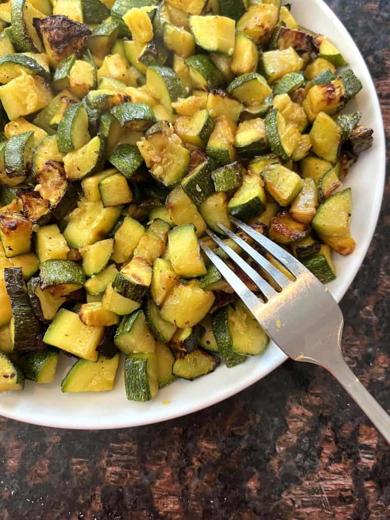 Fork ready to pick up a bite of crispy air fried Lita squash served on a white plate.