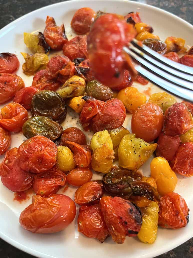 Fork lifting a juicy roasted tomato from a plate of colorful air fried medley tomatoes, highlighting the delicious results.