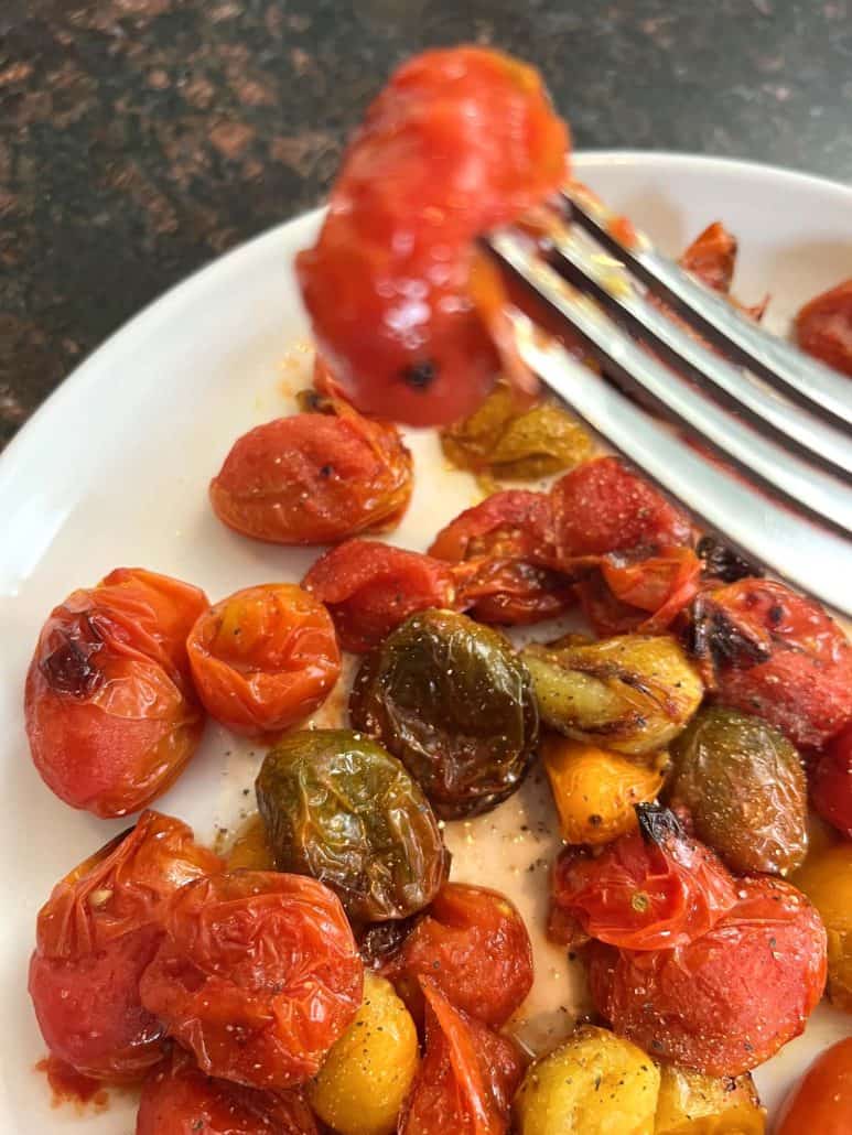 Fork holding a roasted tomato over a plate of blistered medley tomatoes, showcasing the texture and doneness from the air fryer.